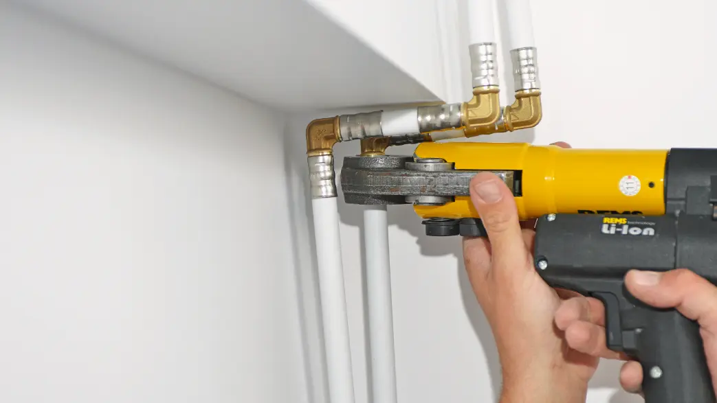 Image d'un professionnel qui sertit un raccord multicouche sur un tube à l'aide d'une sertisseuse hydraulique